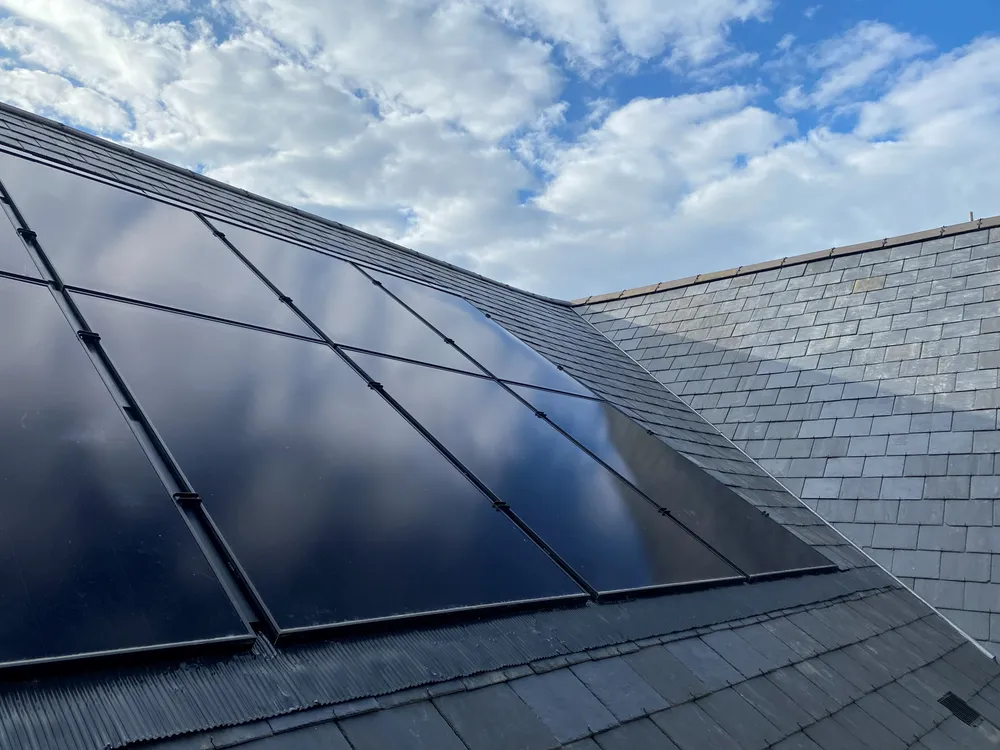 Solar panels mounted above a slate roof against the sky